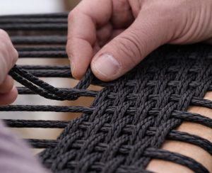 Flechter flechtet eine Stuhlsitzfläche mit schwarzer dänischer Papierschnur in Handarbeit