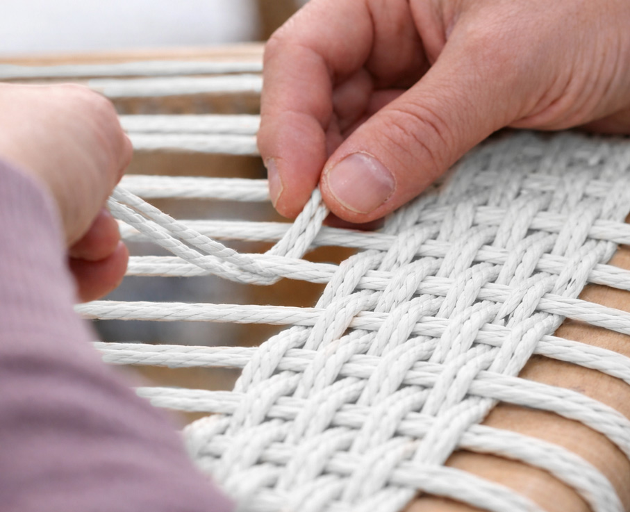 Flechter flechtet eine Stuhlsitzfläche mit weißer dänischer Papierschnur in Handarbeit